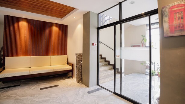 A modern lobby with a wooden slatted wall, a white sofa, a patterned column, and a glass door leading to a staircase. - Aliria Bed and Breakfast (Tagbilaran)