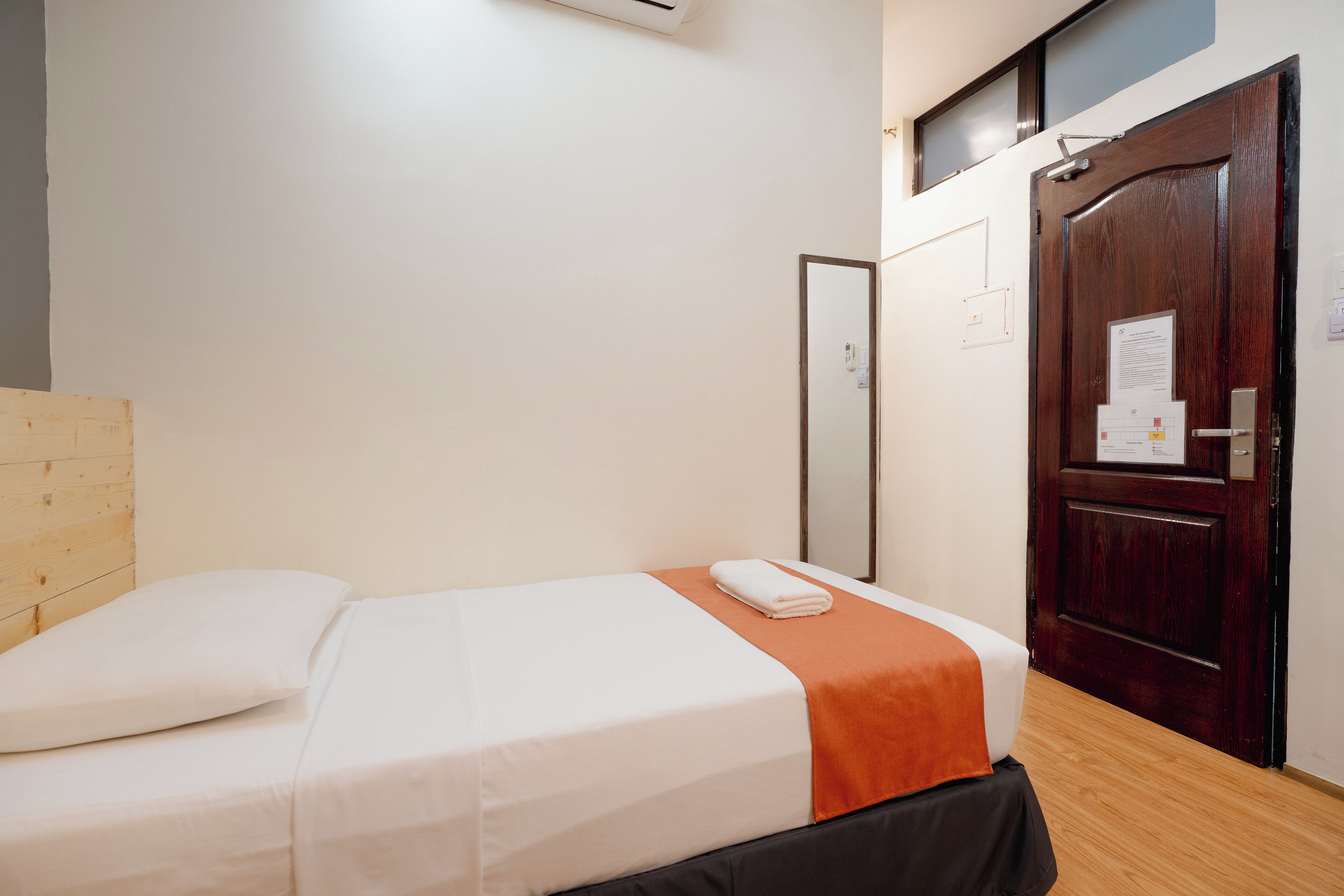 A neatly made bed with a white and orange bedspread, a wooden headboard, and a wooden floor.