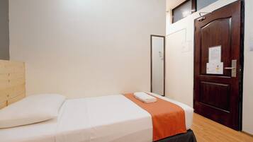 A neatly made bed with a white and orange bedspread, a wooden headboard, and a wooden floor.