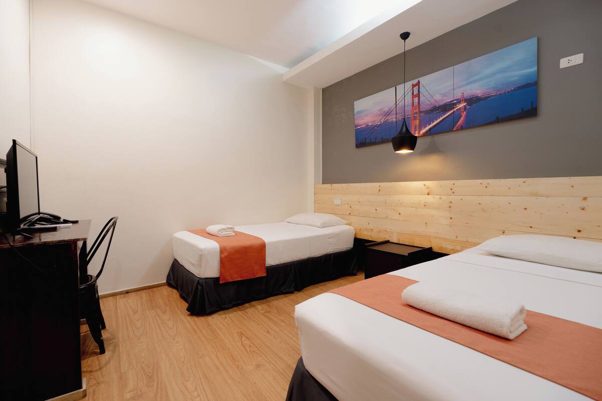 A hotel room with two beds, a desk, and a large painting of a bridge.