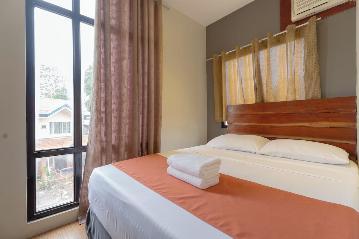 A hotel room with a large window, a bed with white linens, and a wooden headboard.