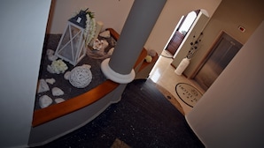 A hotel lobby with a marble floor, a reception desk, a large pillar, and a door leading to the elevator. - Hotel Joy (Castel Volturno)