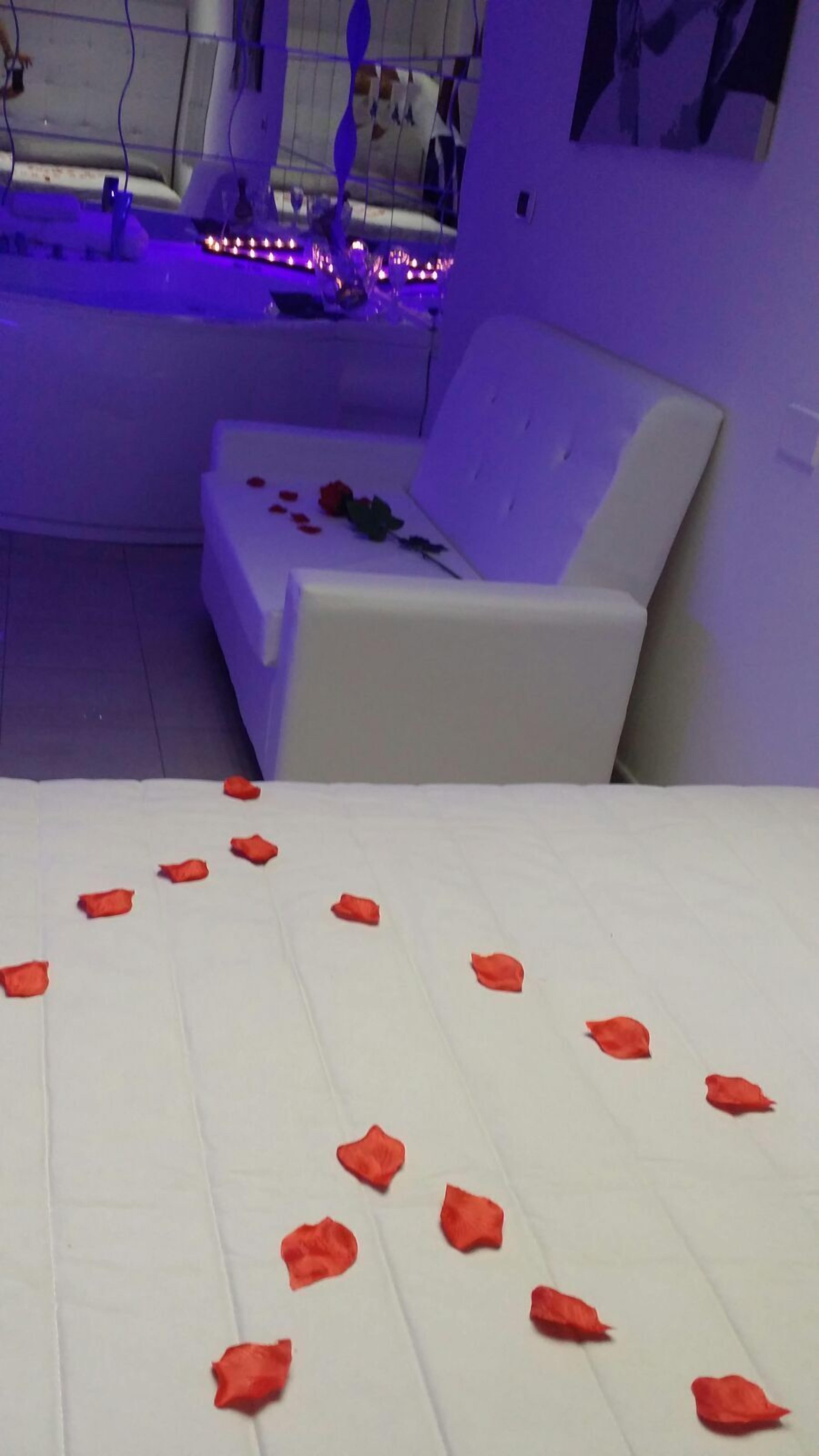 Een kamer met een wit bed, een witte bank en een massagetafel met paars licht.