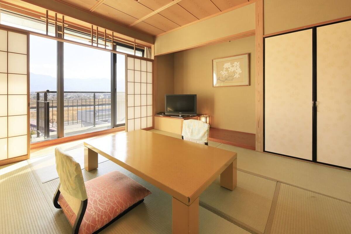 A traditional Japanese room with tatami flooring, a low table, a cushioned bench, a television, and a sliding door.