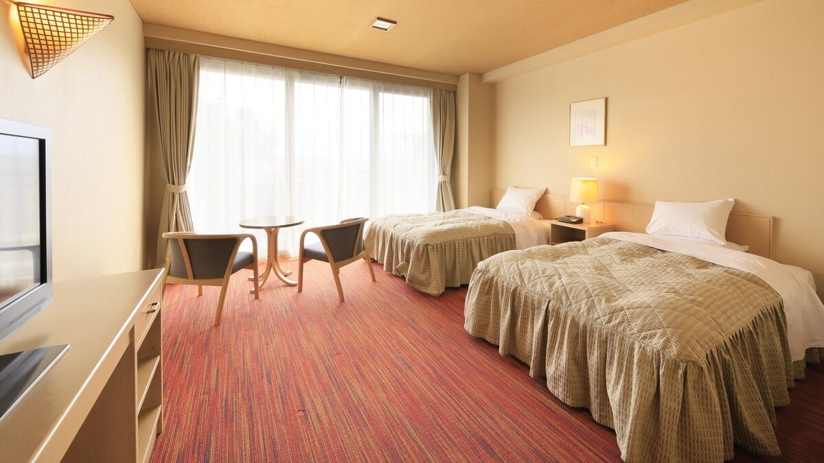 A hotel room with two beds, a desk, a chair, a TV, and a window with curtains.