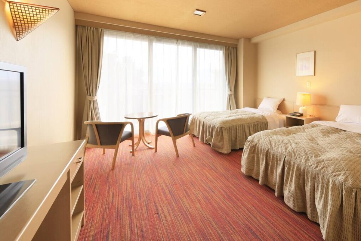 A hotel room with two beds, a desk, a chair, a TV, and a window with curtains.