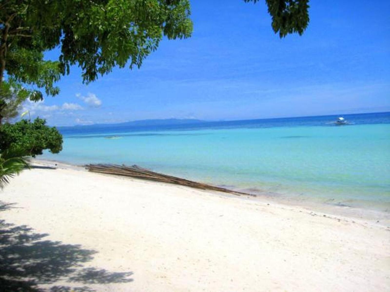 Une plage avec une eau turquoise et limpide, un rivage sablonneux et un bateau à l’horizon.