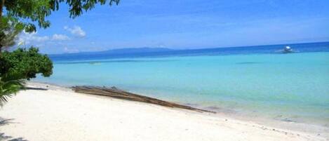 Une plage avec une eau turquoise et limpide, un rivage sablonneux et un bateau à l’horizon.
