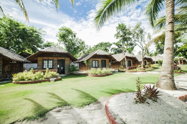 A resort with thatched-roof huts, well-maintained lawns, and tropical plants.