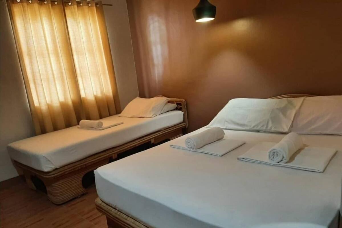 A room with two single beds, each with a rolled towel, a wooden headboard, and a bedside table.