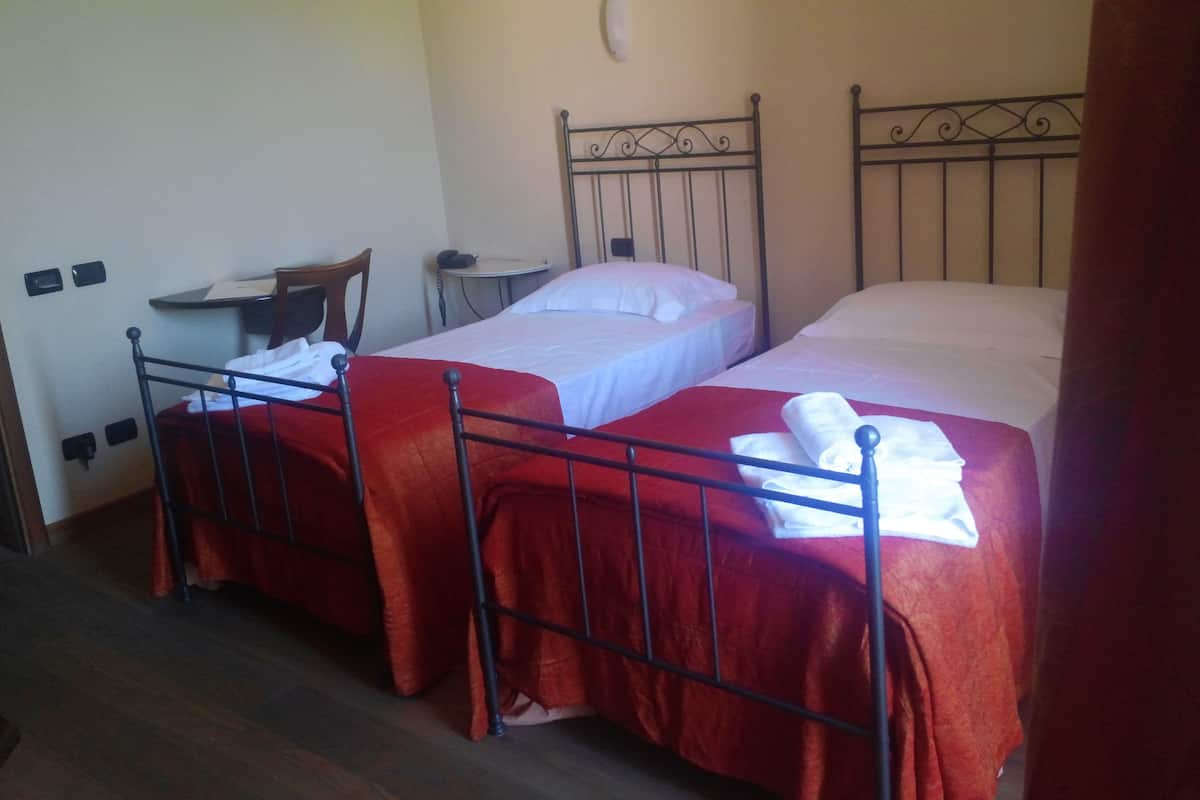 A room with two beds, each with a red bedspread and white linens. There is a small table with a chair and a telephone on the wall.
