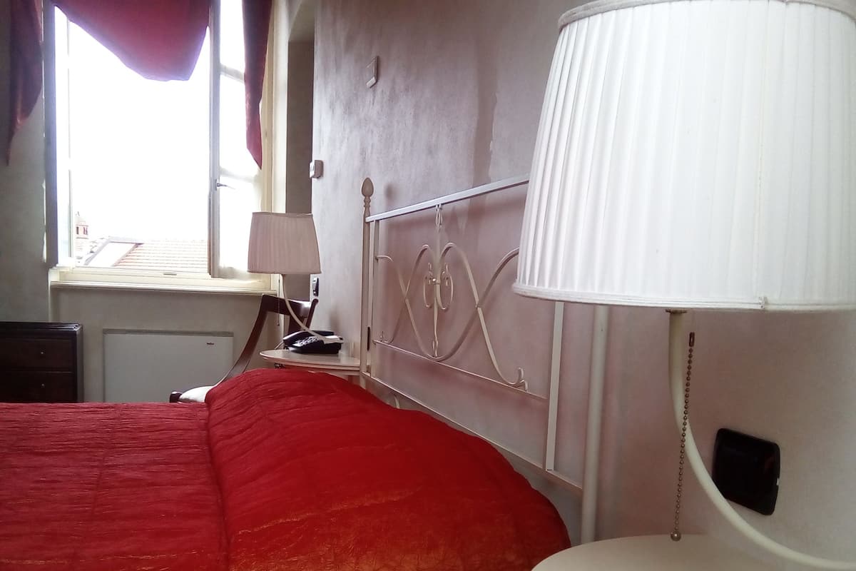 A bedroom with a bed, a bedside table, a lamp, and a window with curtains.