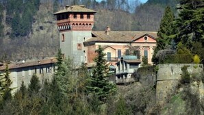 Un bâtiment historique doté d’une tour et d’un corps principal, entouré d’arbres et bordé d’une colline boisée.