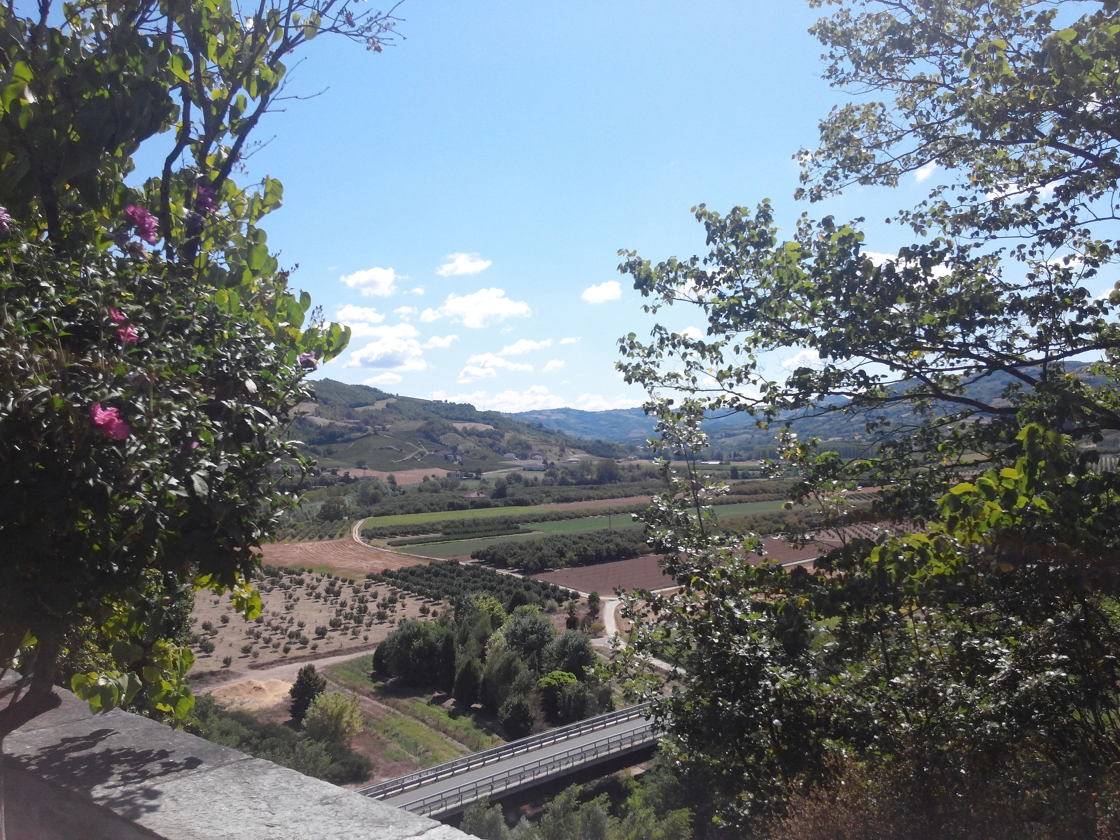 Une vue panoramique depuis un balcon donnant sur une vallée, avec un pont, de la verdure et des collines lointaines.