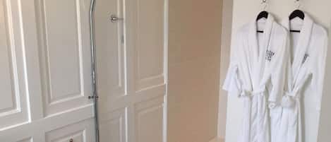 Un baño con inodoro, ducha y dos albornoces blancos colgados en ganchos.
