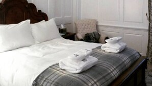 A neatly made bed with white linens, a plaid pillow, and two folded towels on the footboard. - Islay House (Islay Island)