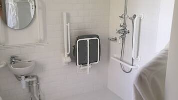 A bathroom with a white sink, a round mirror, a shower with a handheld showerhead, and a grab bar.