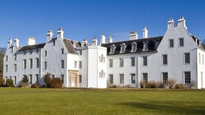 A large, white, multi-story building with a symmetrical facade, multiple chimneys, and a central entrance. - Islay House (Islay Island)