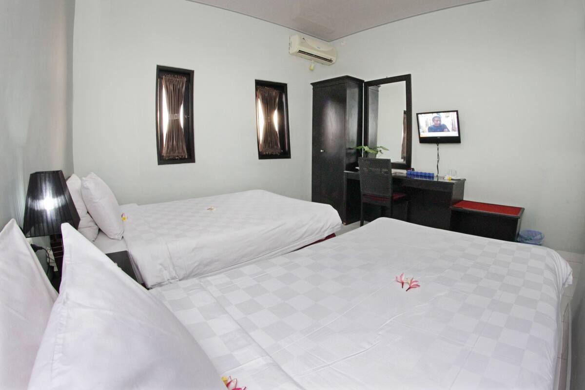 Ein Hotelzimmer mit zwei Betten, einem Schreibtisch, einem Sessel, einem Fernseher und einer Klimaanlage.