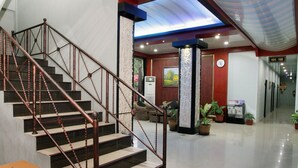 A modern hotel lobby with a staircase, a reception desk, and potted plants. - Shunda Hotel Bali (Denpasar)