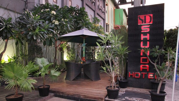 A hotel entrance with a wooden deck, potted plants, and a sign for 'SHUNDA HOTEL'. - Shunda Hotel Bali (Denpasar)