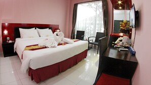 A hotel room with a large bed, a desk with a chair, a TV, and an air conditioning unit. - Shunda Hotel Bali (Denpasar)