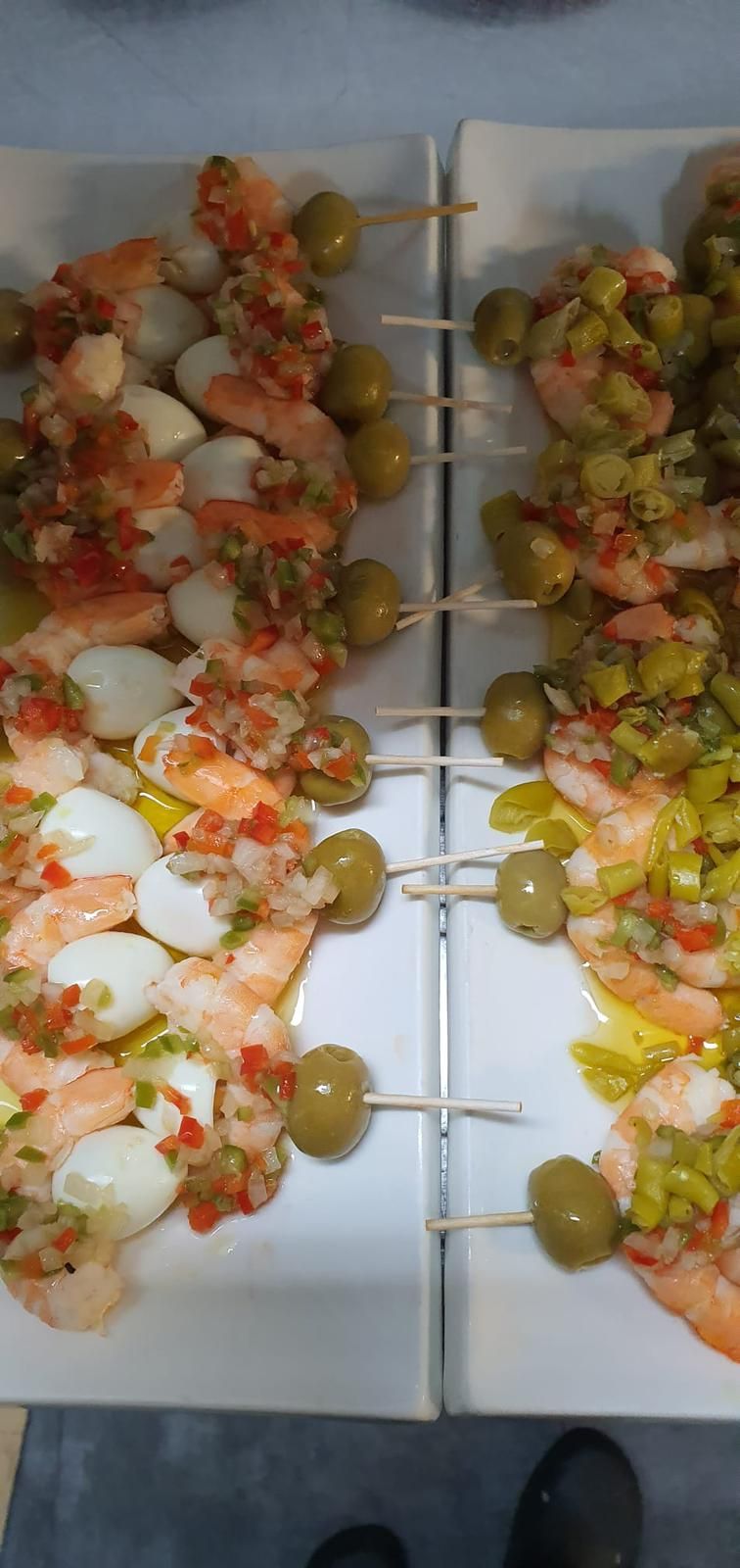 Una mesa con brochetas de camarones y aceitunas.