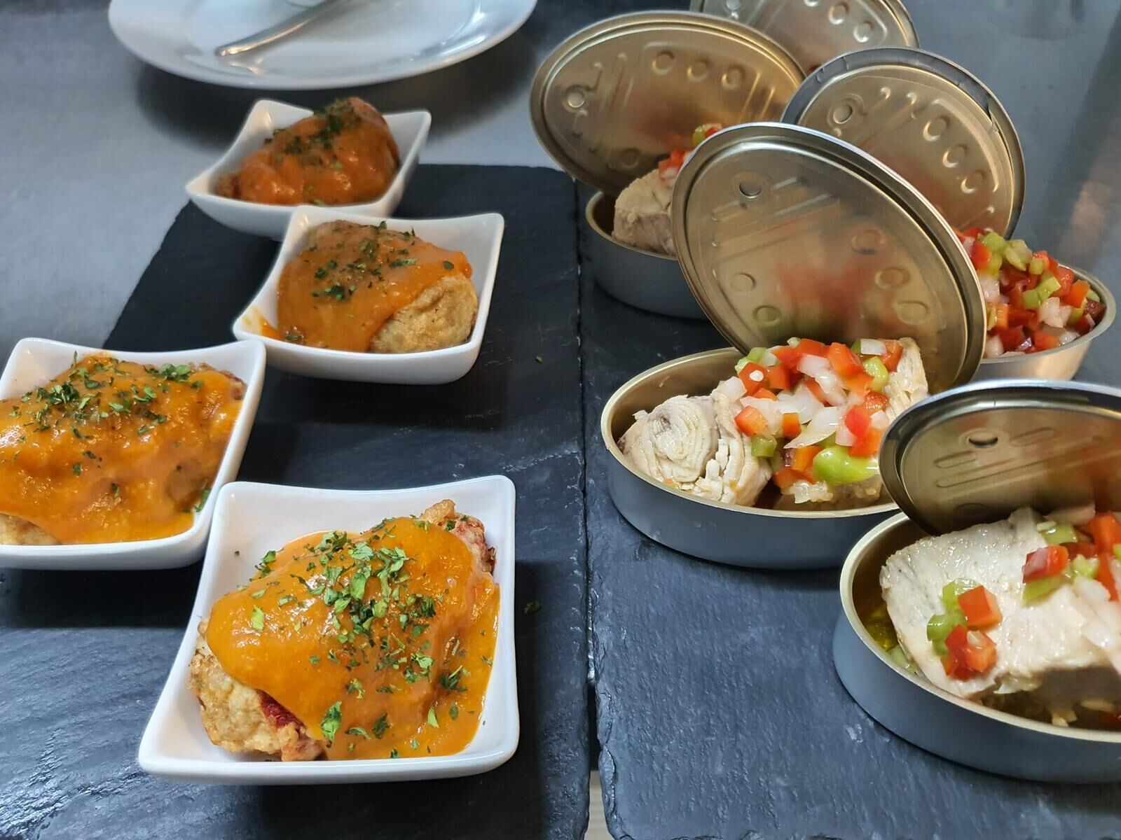 A table with various dishes, including a chicken dish with sauce and a side of diced vegetables.