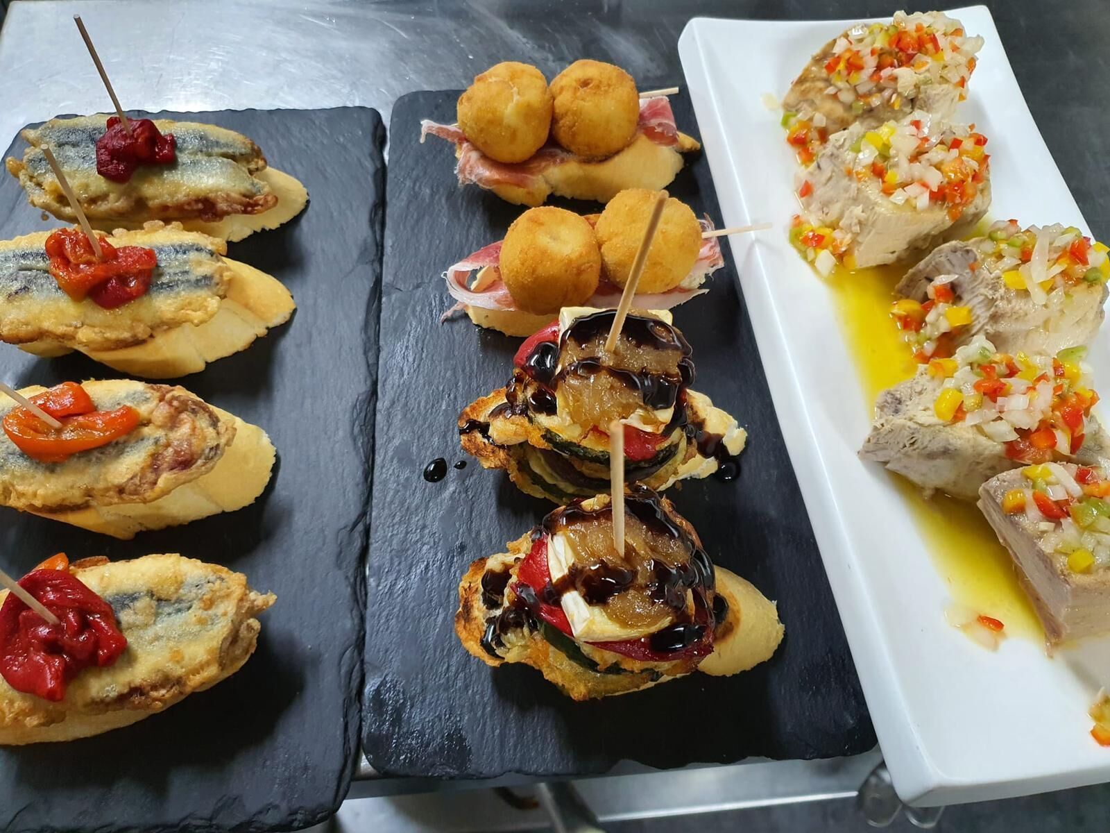 Un assortiment d’amuse-gueule comprenant du poisson, des croquettes et des brochettes, servis sur une planche en ardoise.