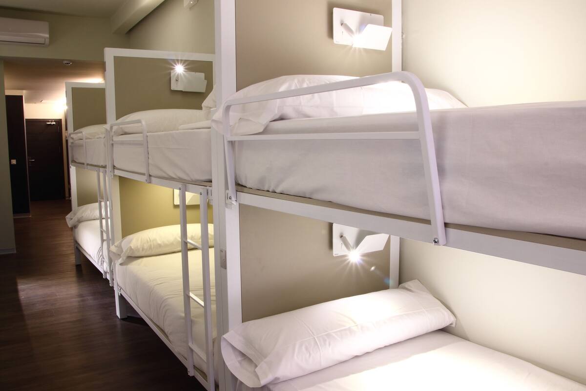 Une chambre avec un lit superposé, du linge de lit blanc et un plancher en bois.