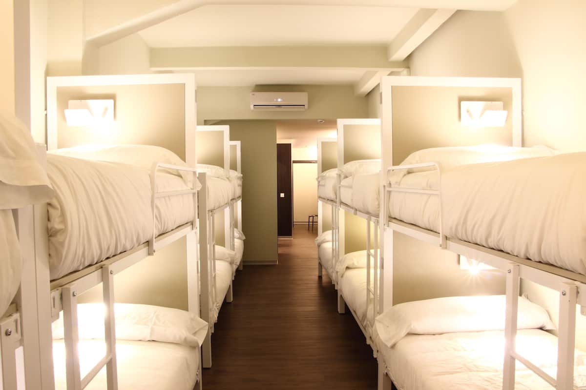 Un couloir avec des lits superposés, chacun étant équipé d’un matelas et d’un oreiller blancs, et un appareil de climatisation installé au-dessus.