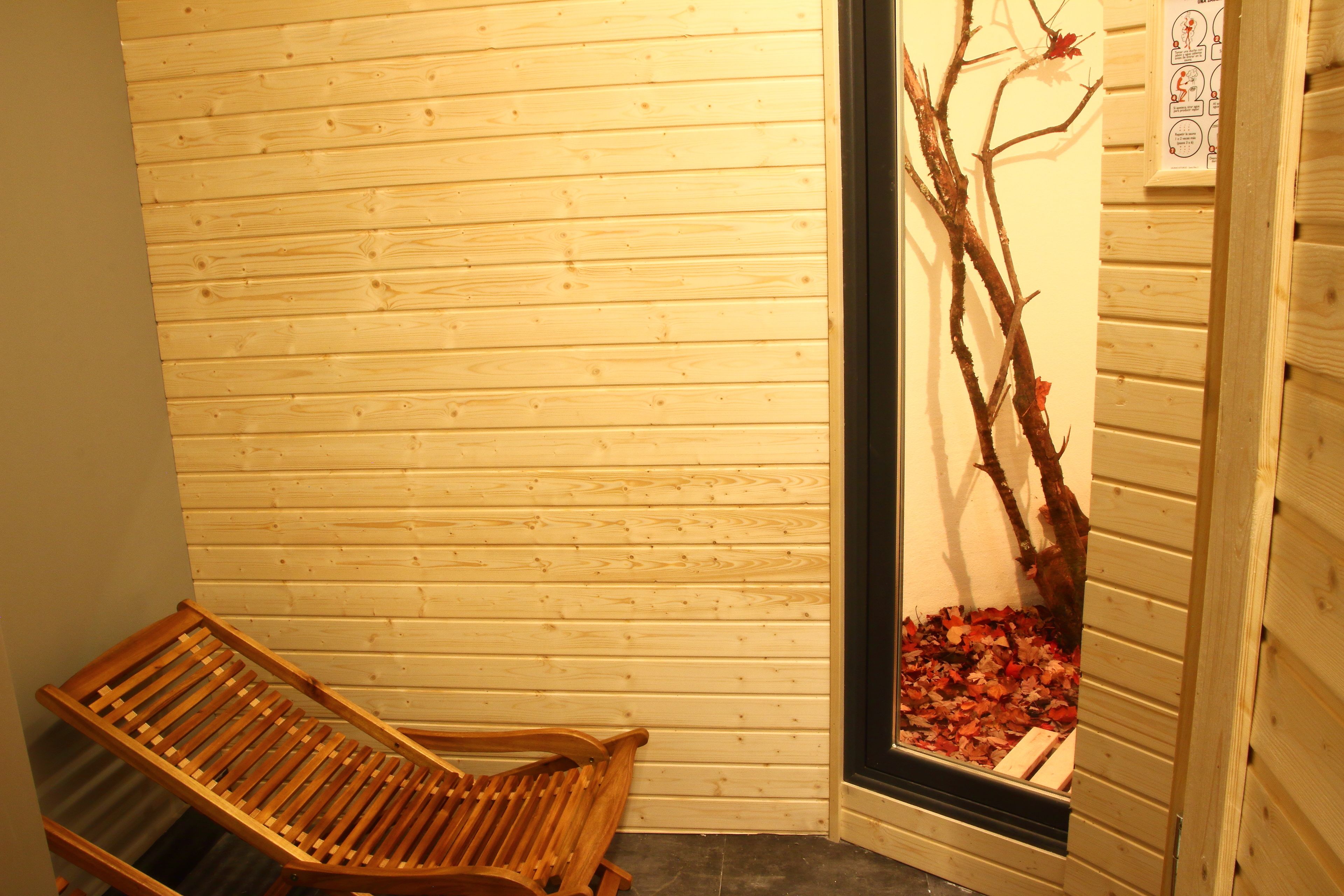 Un banco de madera en un rincón, con una pared de madera y una ventana con una rama y hojas.