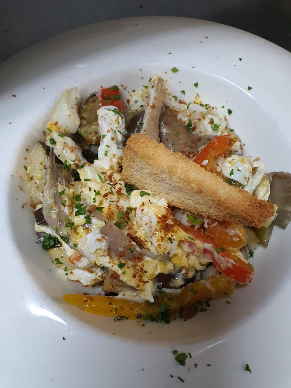 Un plato con diversos ingredientes, entre ellos vegetales y posiblemente mariscos, decorado con hierbas.