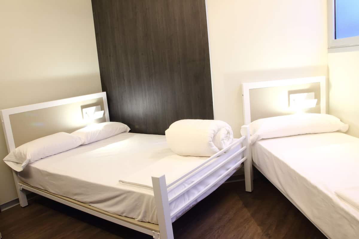 Deux lits simples avec du linge de lit blanc et des têtes de lit, un panneau en bois foncé sur le mur et une fenêtre laissant entrer la lumière du jour.