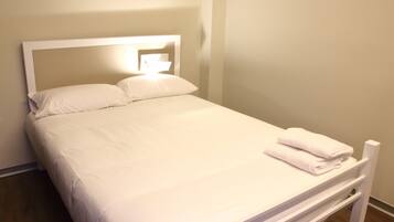 A neatly made bed with white linens and pillows, a white headboard, and a folded towel on the footboard.