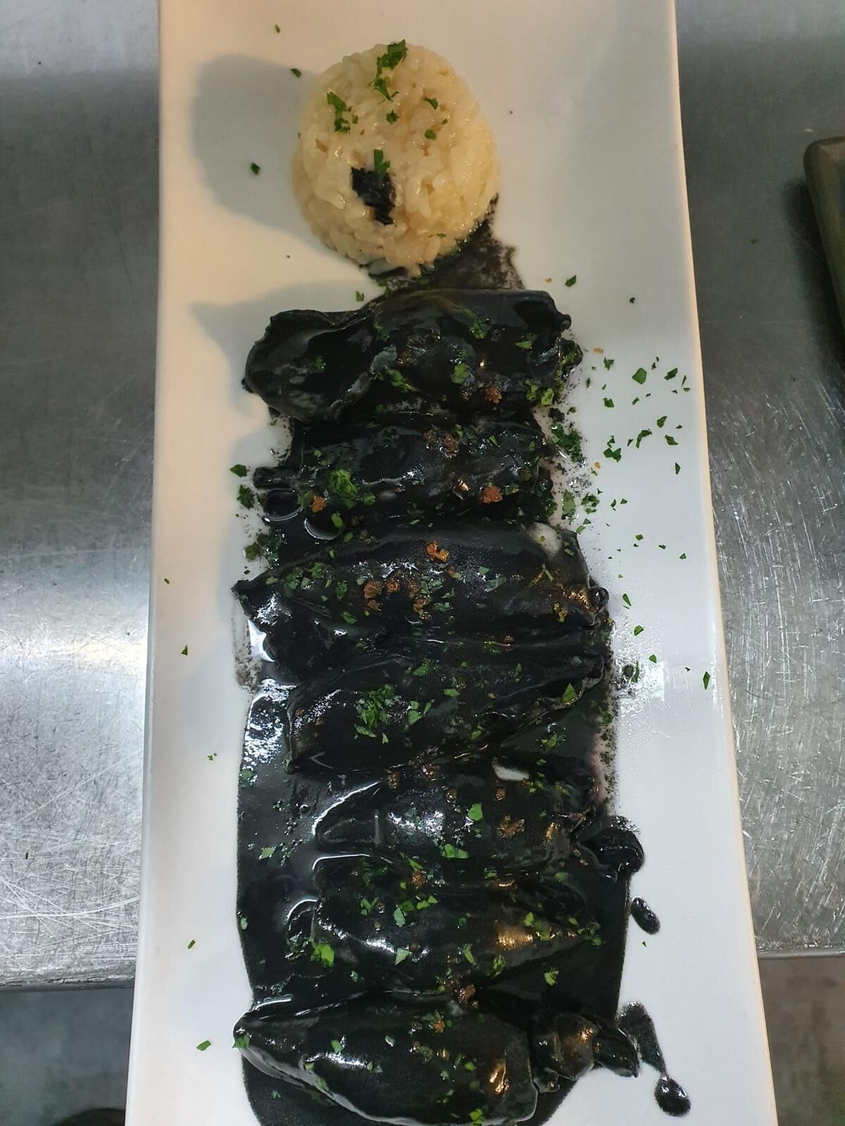 A plate with a dark sauce-covered dish and a mound of rice garnished with herbs.
