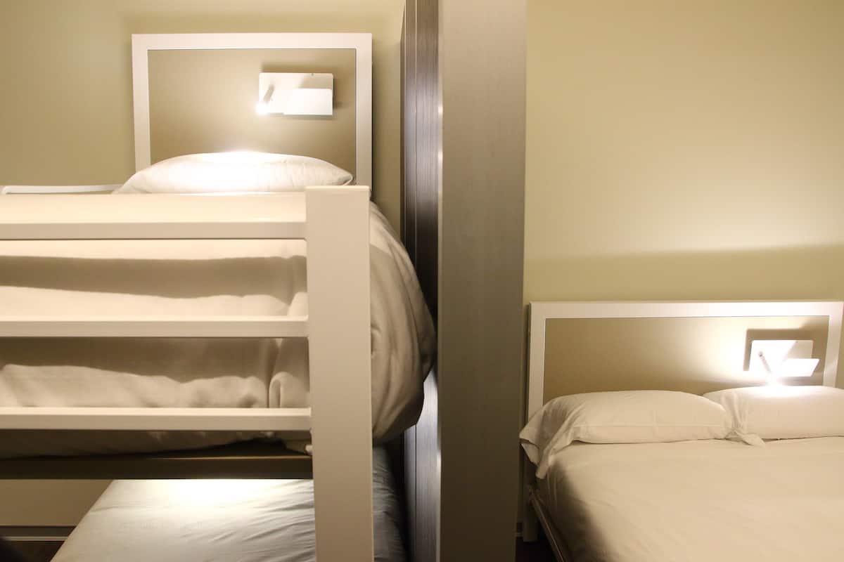 Une chambre d’hôtel avec des lits superposés et un lit simple, tous deux dotés de draps blancs.