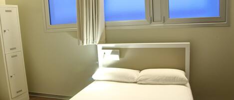 A bedroom with a bed, a window with curtains, and a white wardrobe.