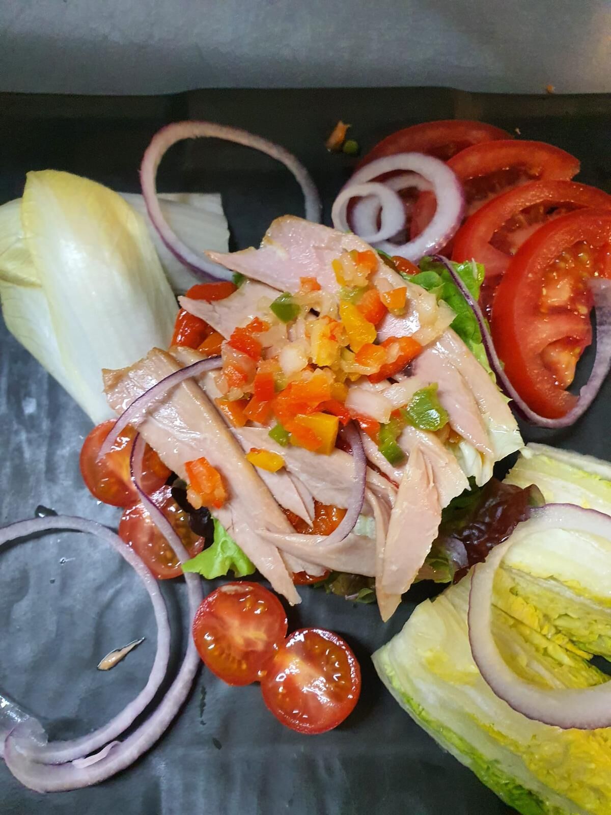 Insalata con verdure miste e pollo su un piatto scuro.