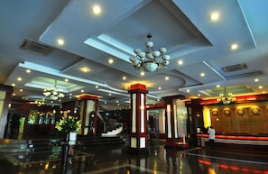 A spacious lobby with a grand staircase, multiple chandeliers, and a reception desk.