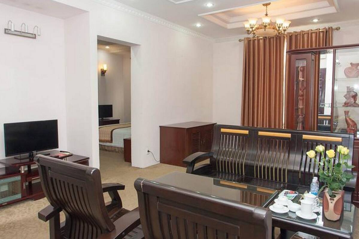 A living room with a television, a dining table with chairs, a chandelier, and a cabinet with decorative items.