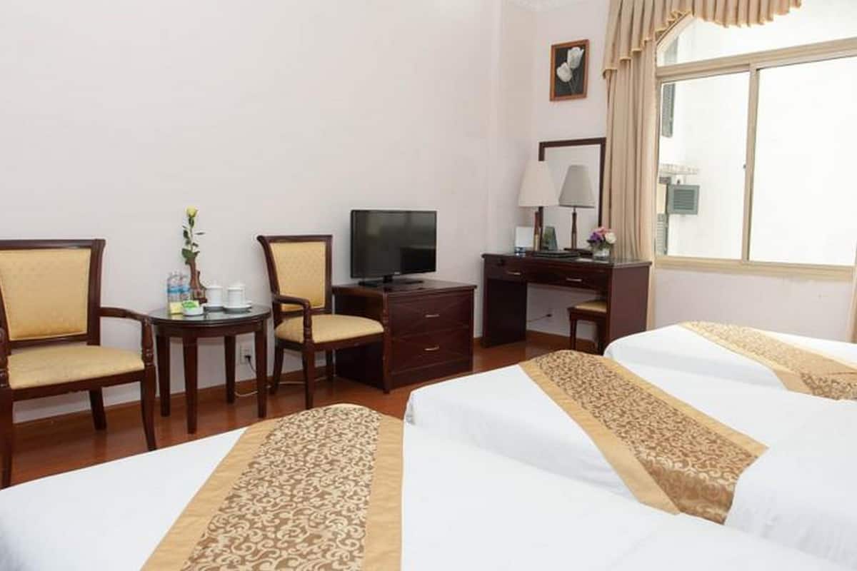 A hotel room with two beds, a desk, a television, and a window with curtains.