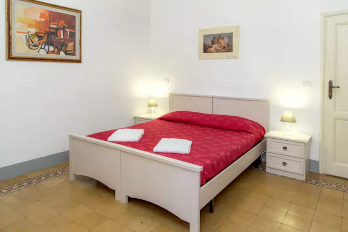 A bedroom with a white bed, red bedding, two bedside tables with lamps, and a door.