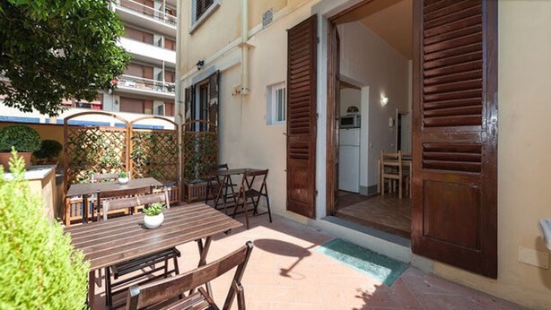 An outdoor patio area with a wooden table and chairs, a small potted plant, and a view into the adjacent building. - L'ARANCETO&STILNOVO GUEST HOUSE DI TOKA ALFONS (Florence)