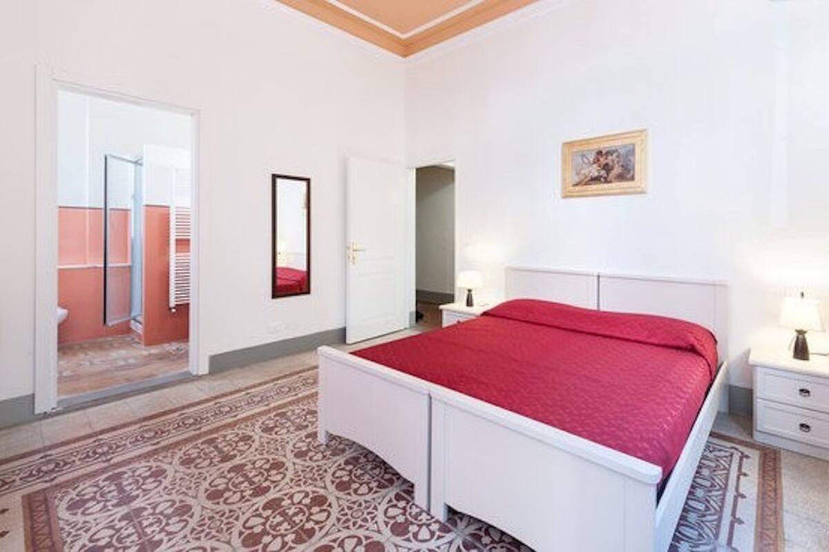 A bedroom with a bed, bedside tables, a mirror, and a door leading to a bathroom.