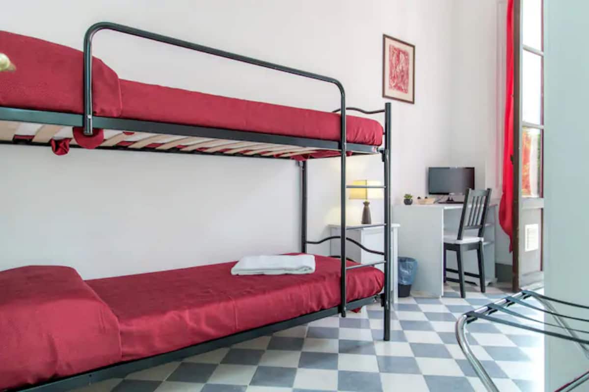 A dormitory room with bunk beds, a desk, a chair, and a television.