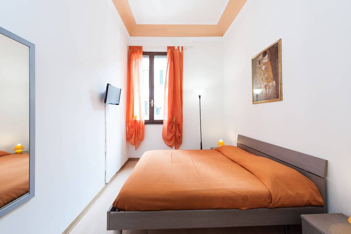 A bedroom with a bed, a TV, a lamp, and a painting on the wall.