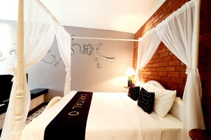 Una cama con dosel y cuatro columnas, con colcha blanco y negro, un mural en la pared y una pared decorada con ladrillos.