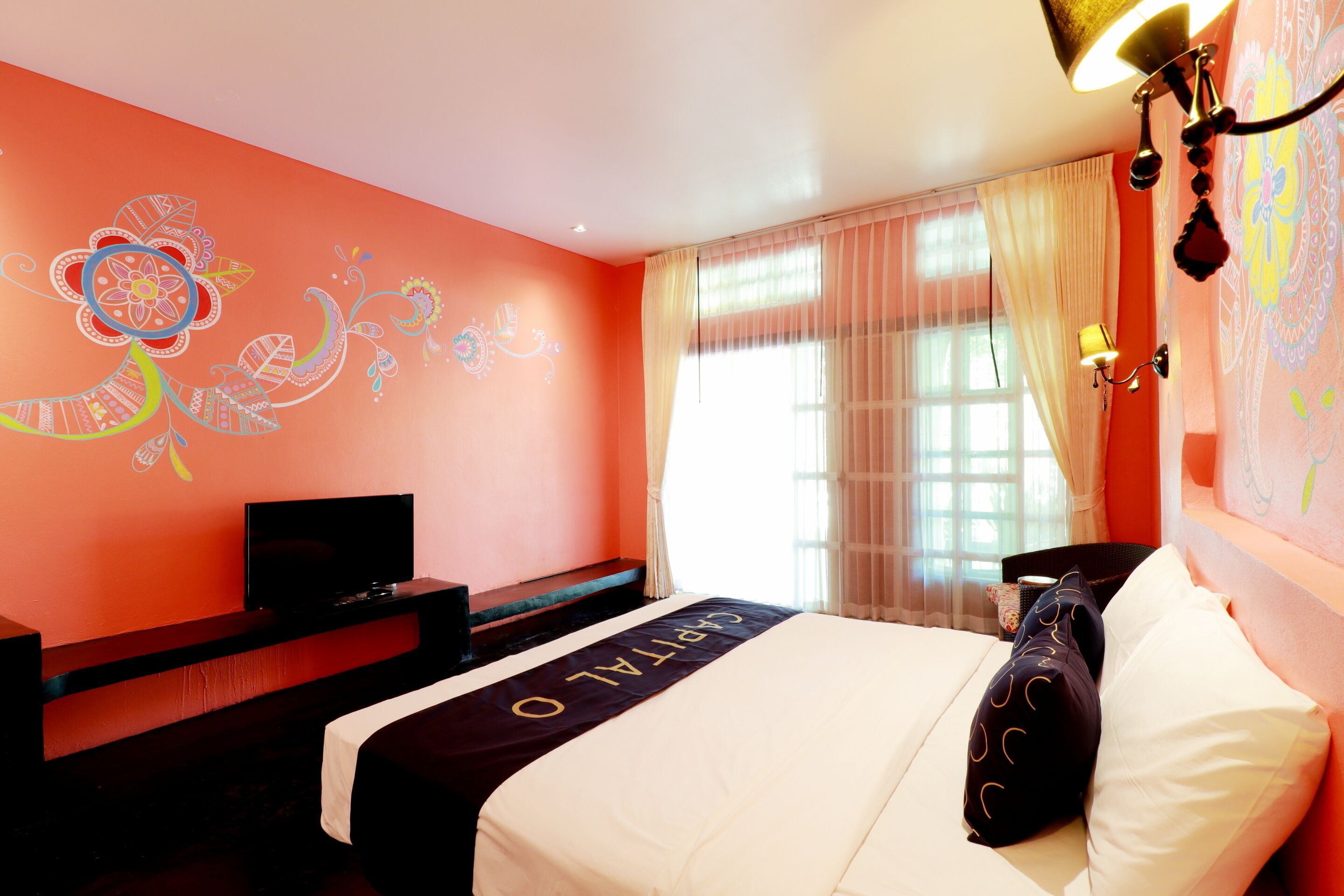 A hotel room with a bed, a TV on a stand, a desk, and a window with curtains.