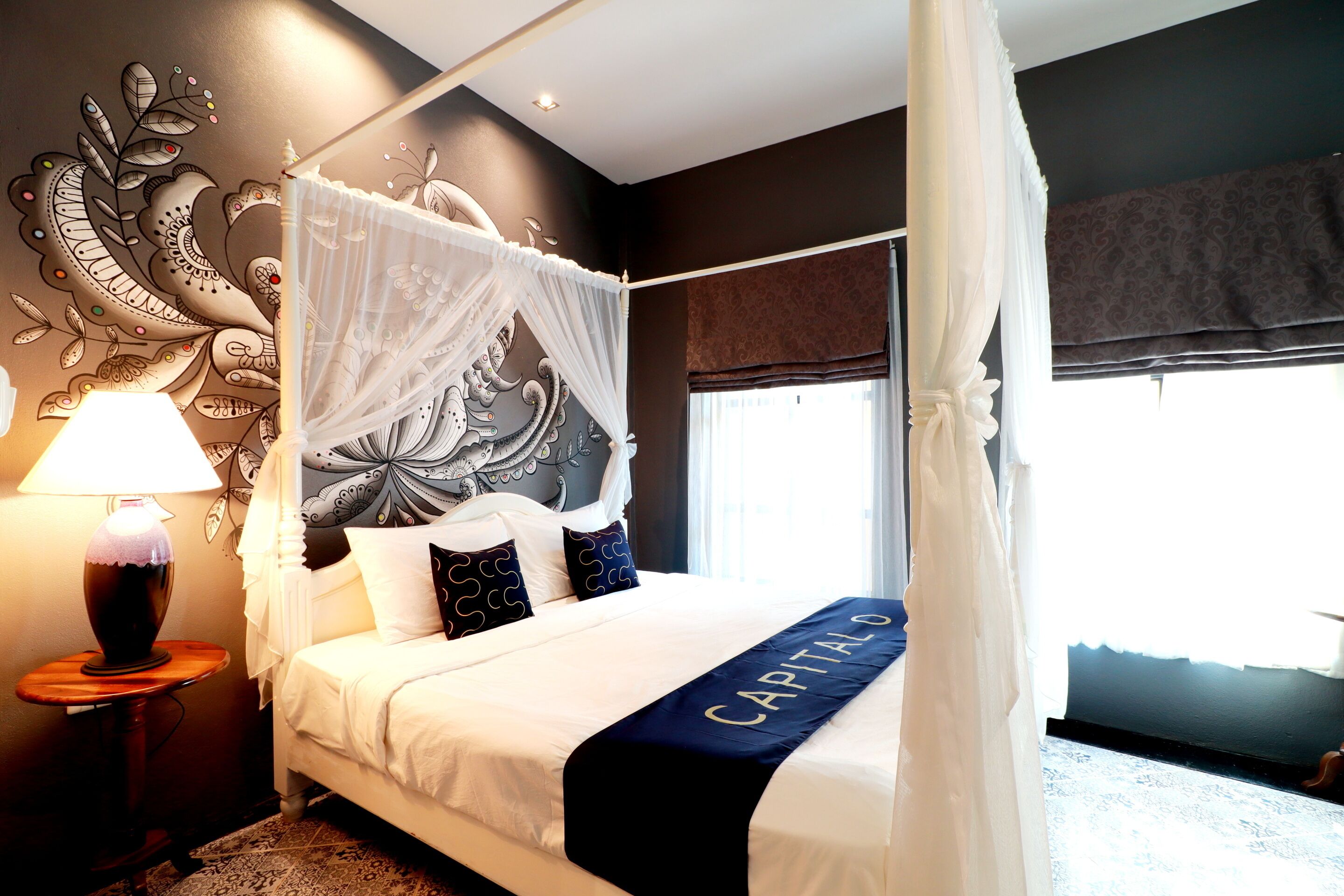 A four-poster bed with a canopy, a bedside table with a lamp, and a decorative wall mural.